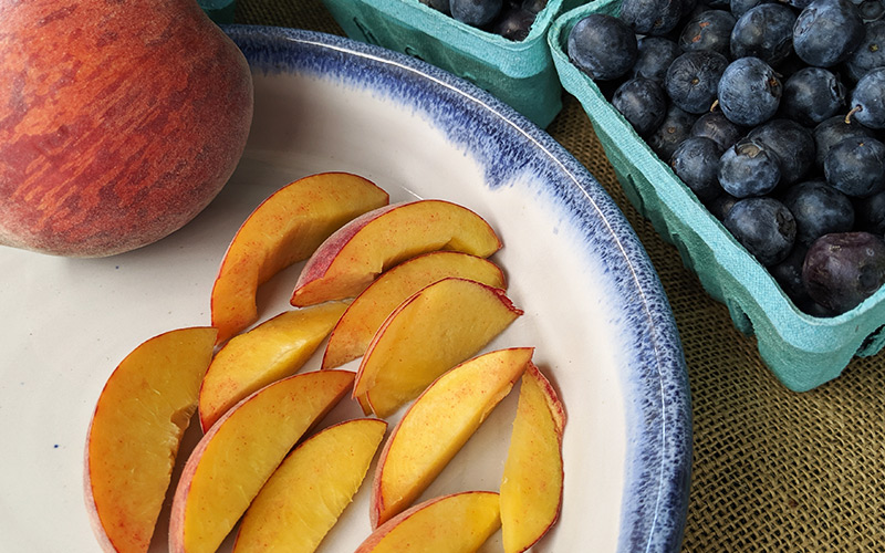 Sliced peaches on a pottery plate next to blueberries